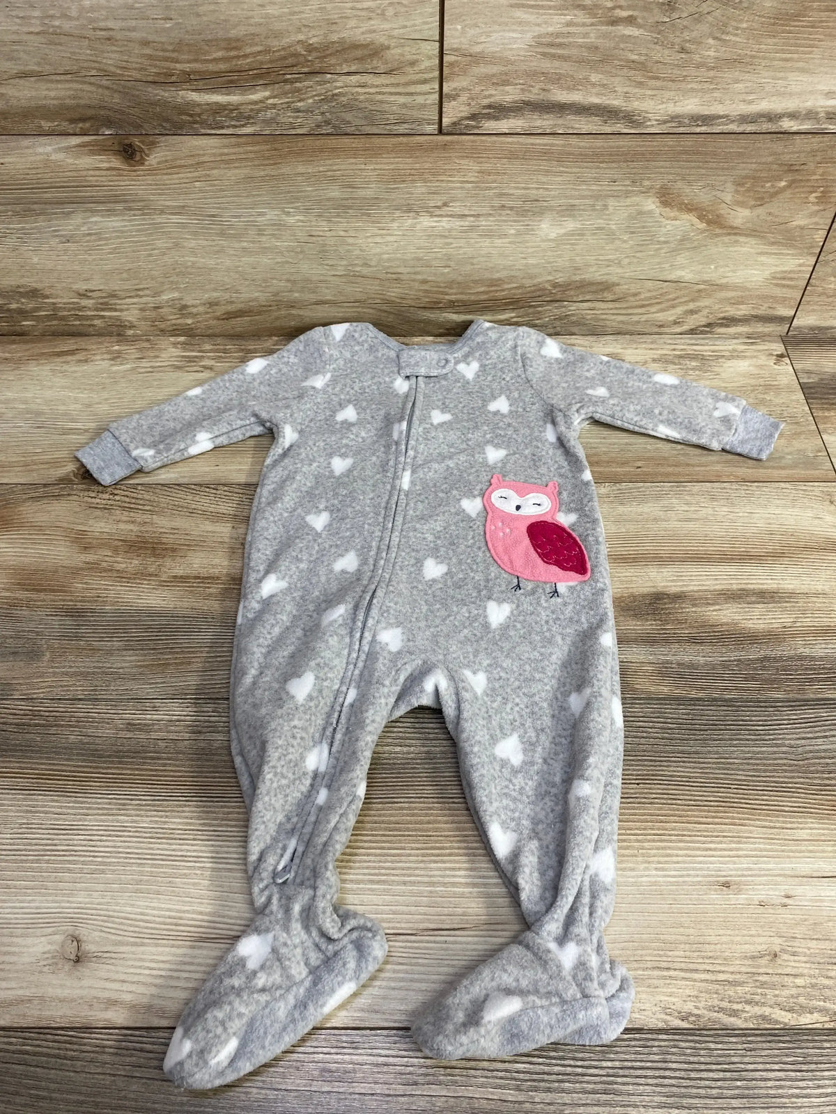 Gray baby footed sleeper with white hearts and a pink owl patch, laid on wood floor