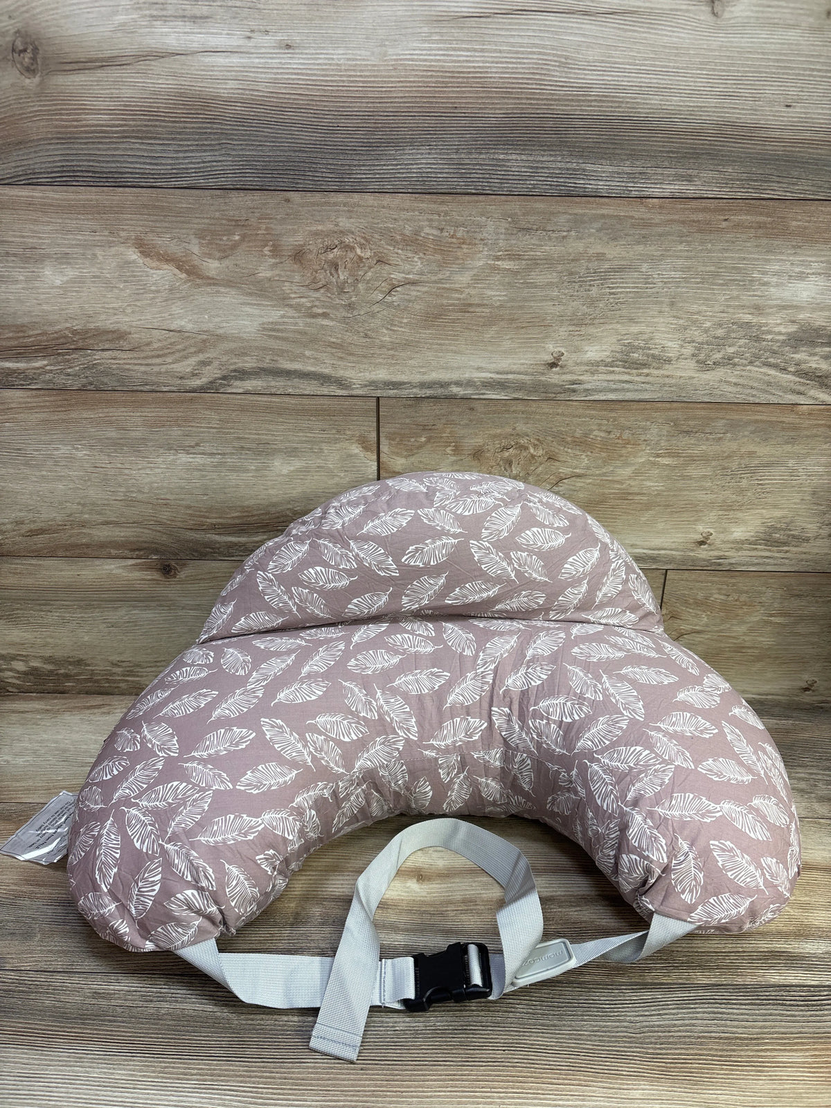 Top view of Momcozy Original adjustable nursing pillow in pink with white leaf pattern, gray strap, and black buckle on wood