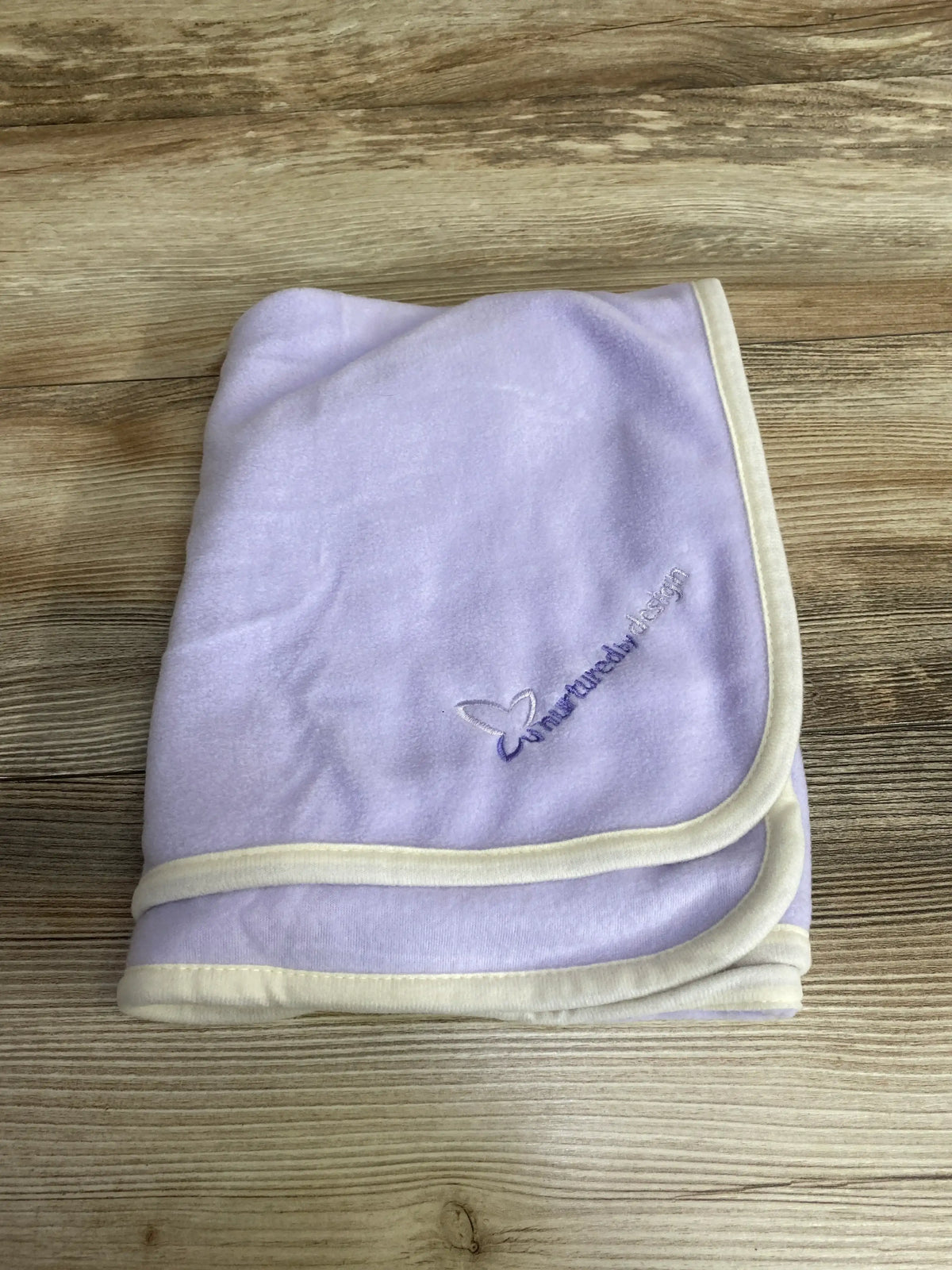 Folded lavender baby blanket with cream trim on wood background