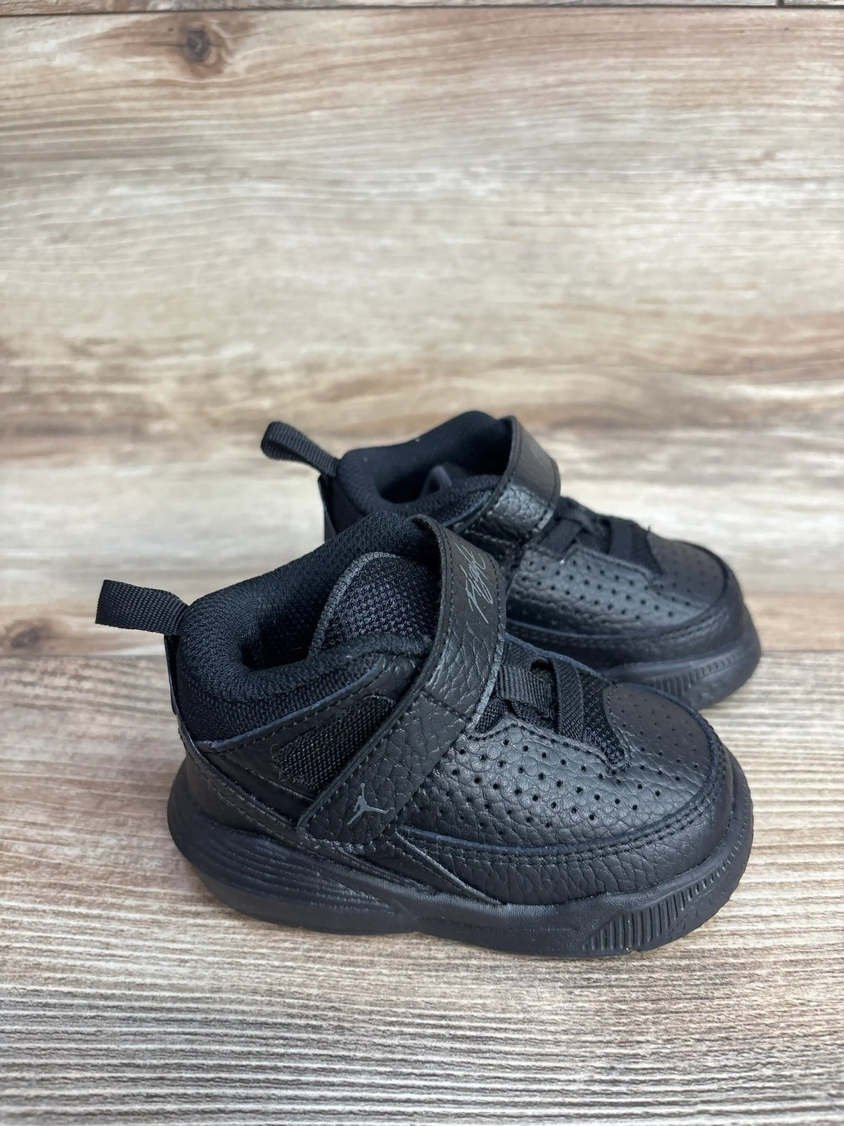 Angled front view of Air Jordan Max Aura 5 TD toddler sneakers 4C black anthracite with Velcro strap and perforated leather on wooden floor