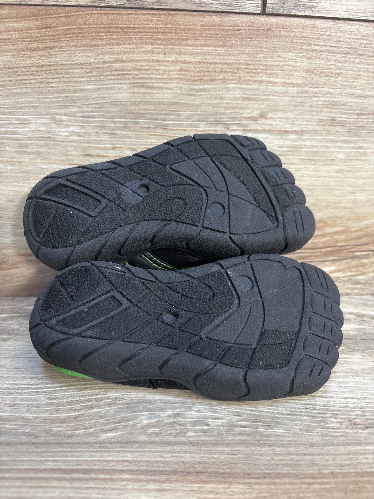 Black rubber soles of kids’ shoes with tread pattern on wood background