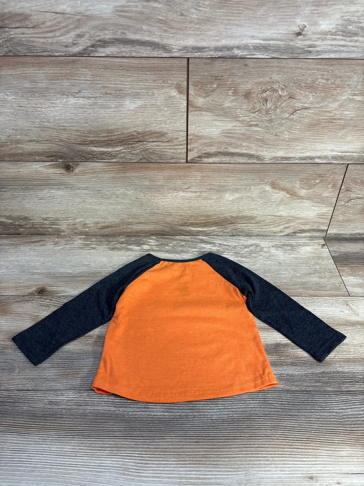 Back view of Jumping Beans Paw Patrol Trick Or Treat shirt with orange body and black raglan sleeves on a wood-look surface