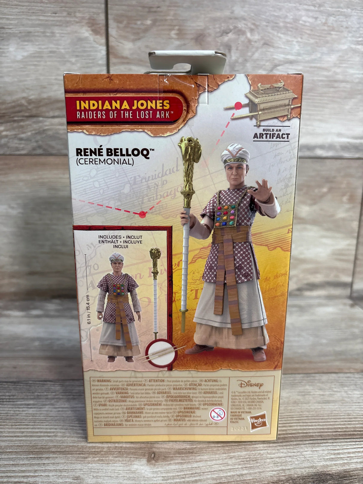 Front view of René Belloq ceremonial action figure in box showcasing the included staff accessory and Raiders of the Lost Ark logo on a wood surface