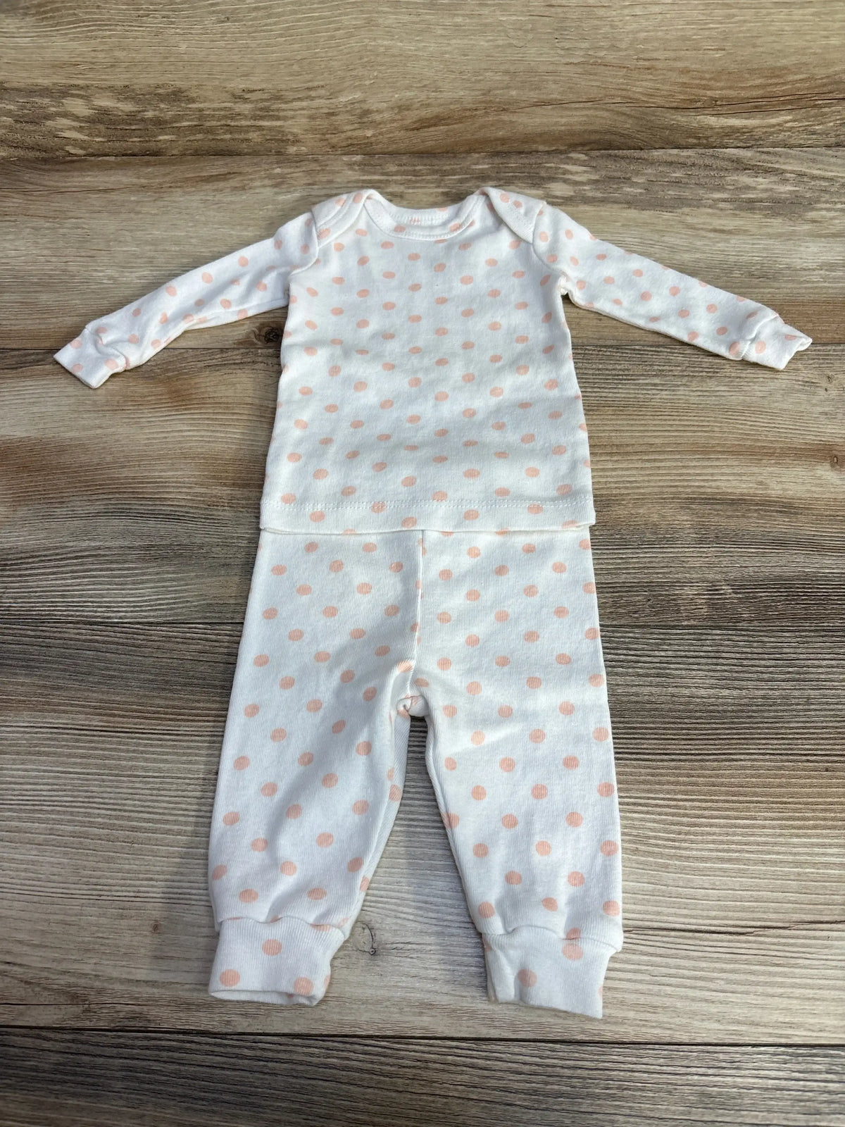 Flat lay of Mighty Goods 2-piece white baby pajama set showing peach polka dots, cuffed ankles on wood background