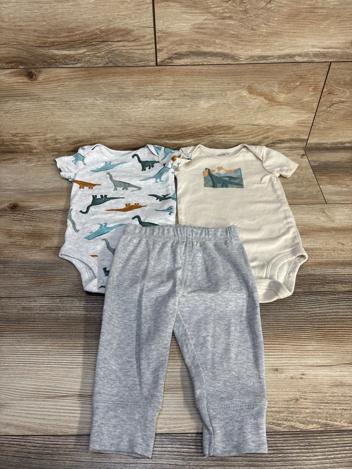 Top view of Child Of Mine three-piece bodysuit and pants set showing dinosaur print and gray pants, size 3 to 6 months