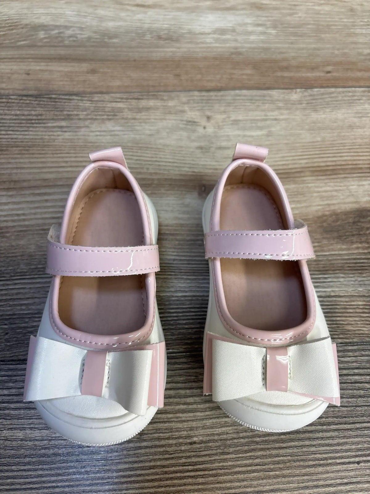 Pink and white baby girl dress shoes with bows on wooden floor
