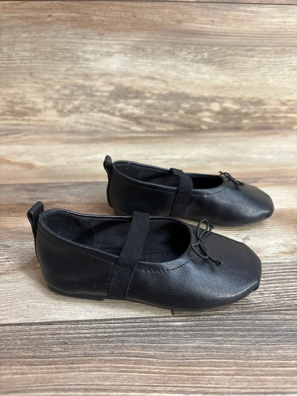 Black leather ballet shoes with elastic straps and bows on wood floor