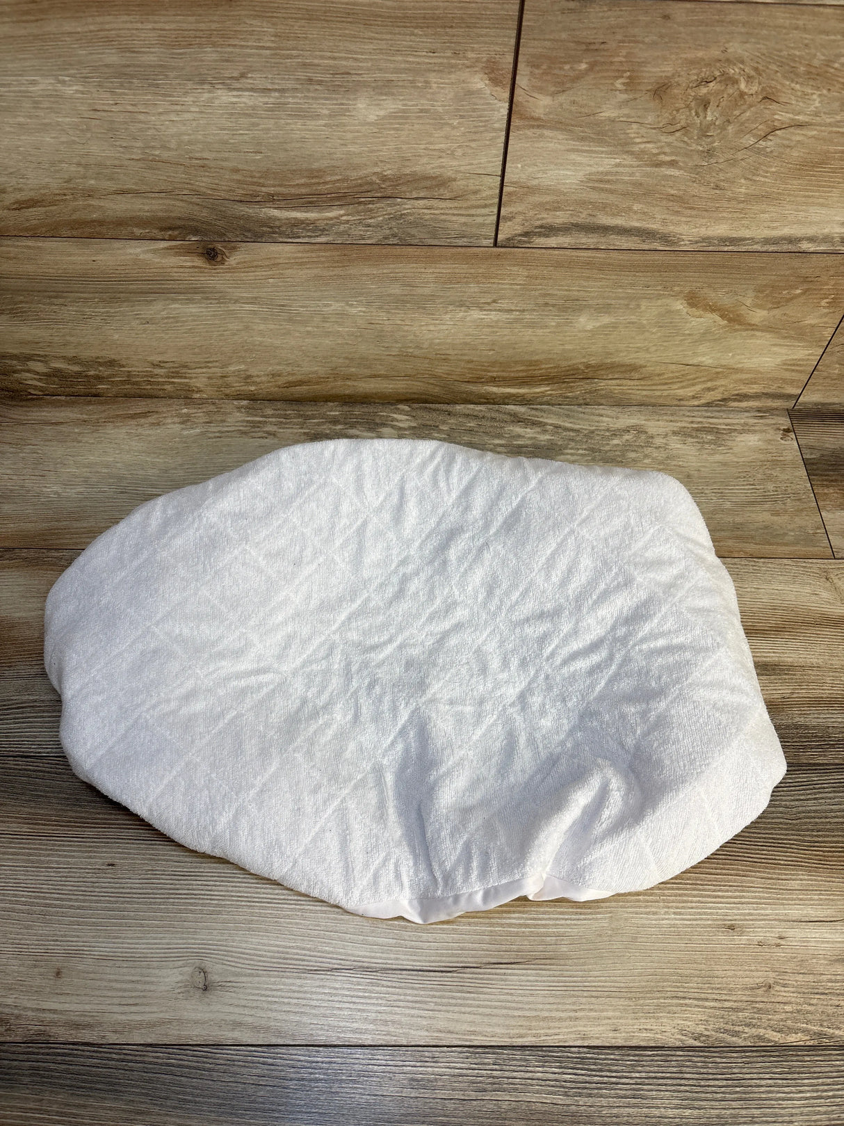 Top-down view of Biloban waterproof quilted bassinet mattress pad cover showing elastic fitted edges and diamond quilting on wood floor
