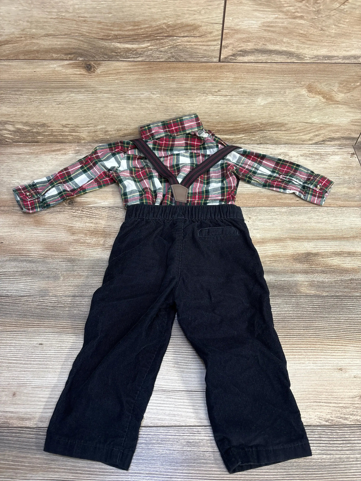 Children's outfit with red and green plaid shirt and black pants with suspenders on wooden floor