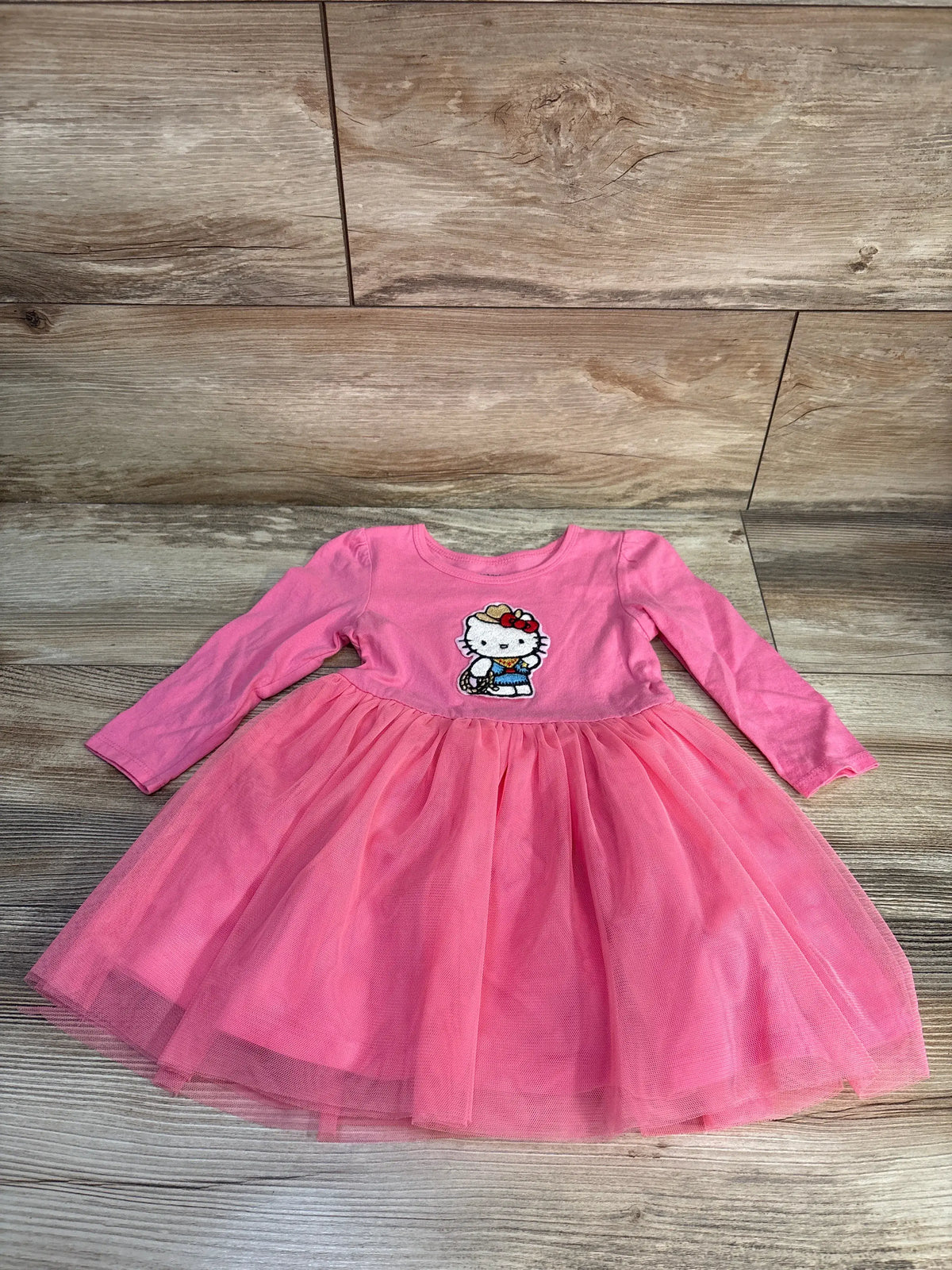 Front view of Carter’s Hello Kitty dress in pink with long sleeves, character design, and full tulle skirt on wood-look floor