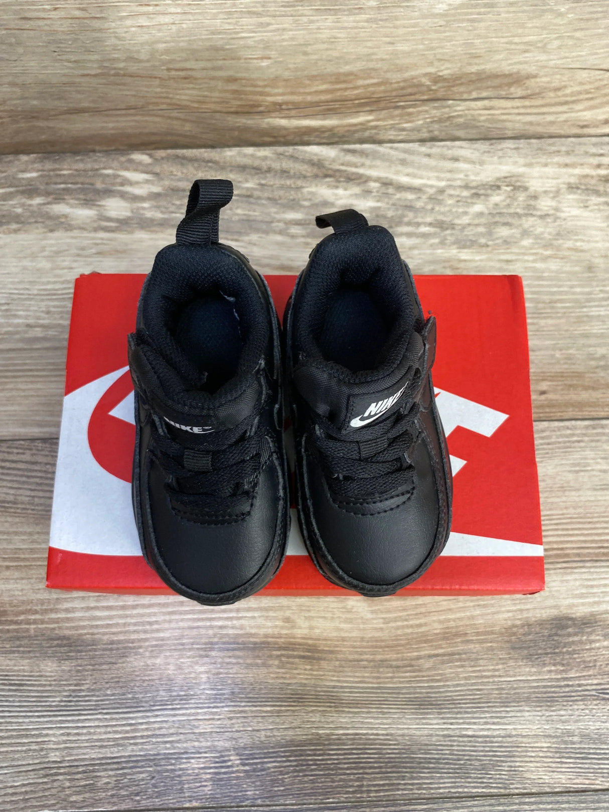 Top-down view of toddler Nike Air Max 90 EasyOn sneakers showing all black leather upper and pull tabs on red Nike box