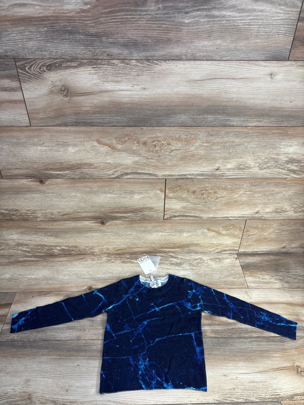 Navy blue kids sweater with electric blue vein-like pattern, laid flat on wooden floor