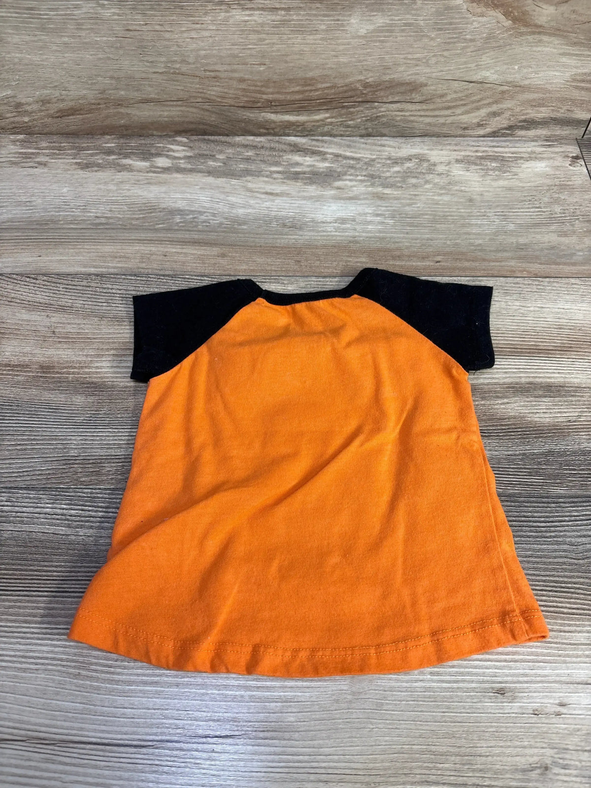 Flat lay of an orange and black Disney Minnie shirt showcasing black sleeves on a wood grain background