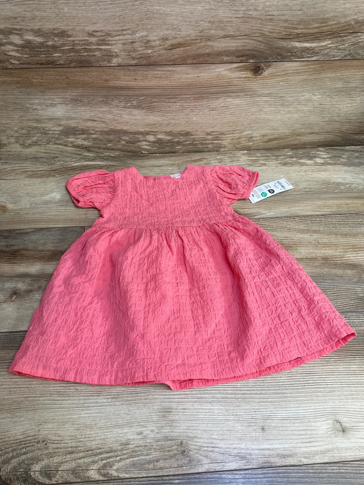 Flat lay of pink baby dress and matching bloomers showcasing puff sleeves and crinkled texture on wood background