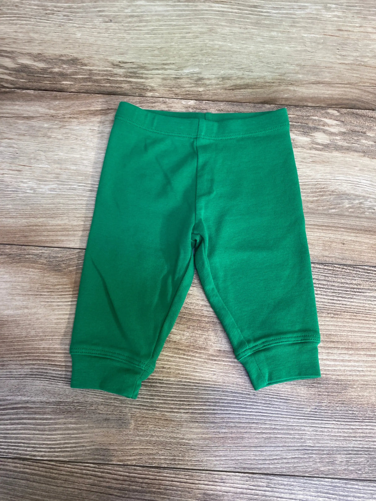Flat lay of Primary pull-on baby pants in green (0–3M) showing elastic waistband and cuffed ankles on wood background