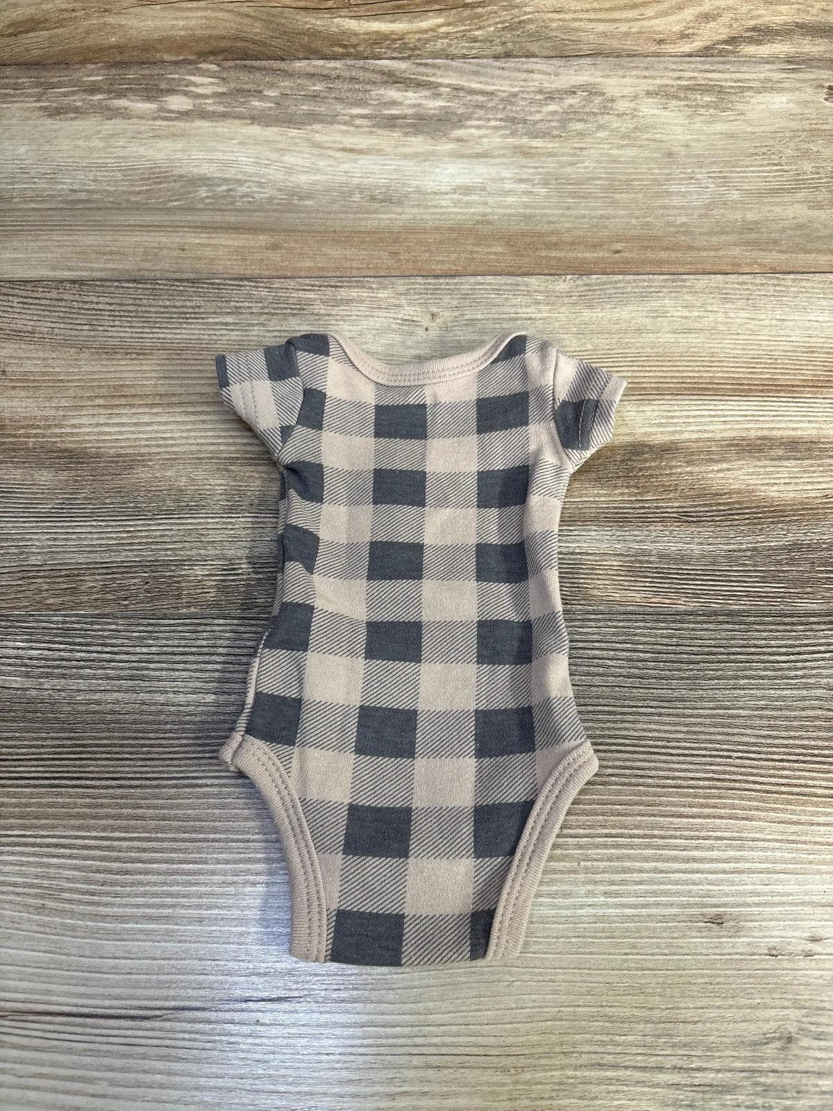 Front view of Hudson Baby bodysuit showcasing a tan and dark gray plaid pattern with a wood background