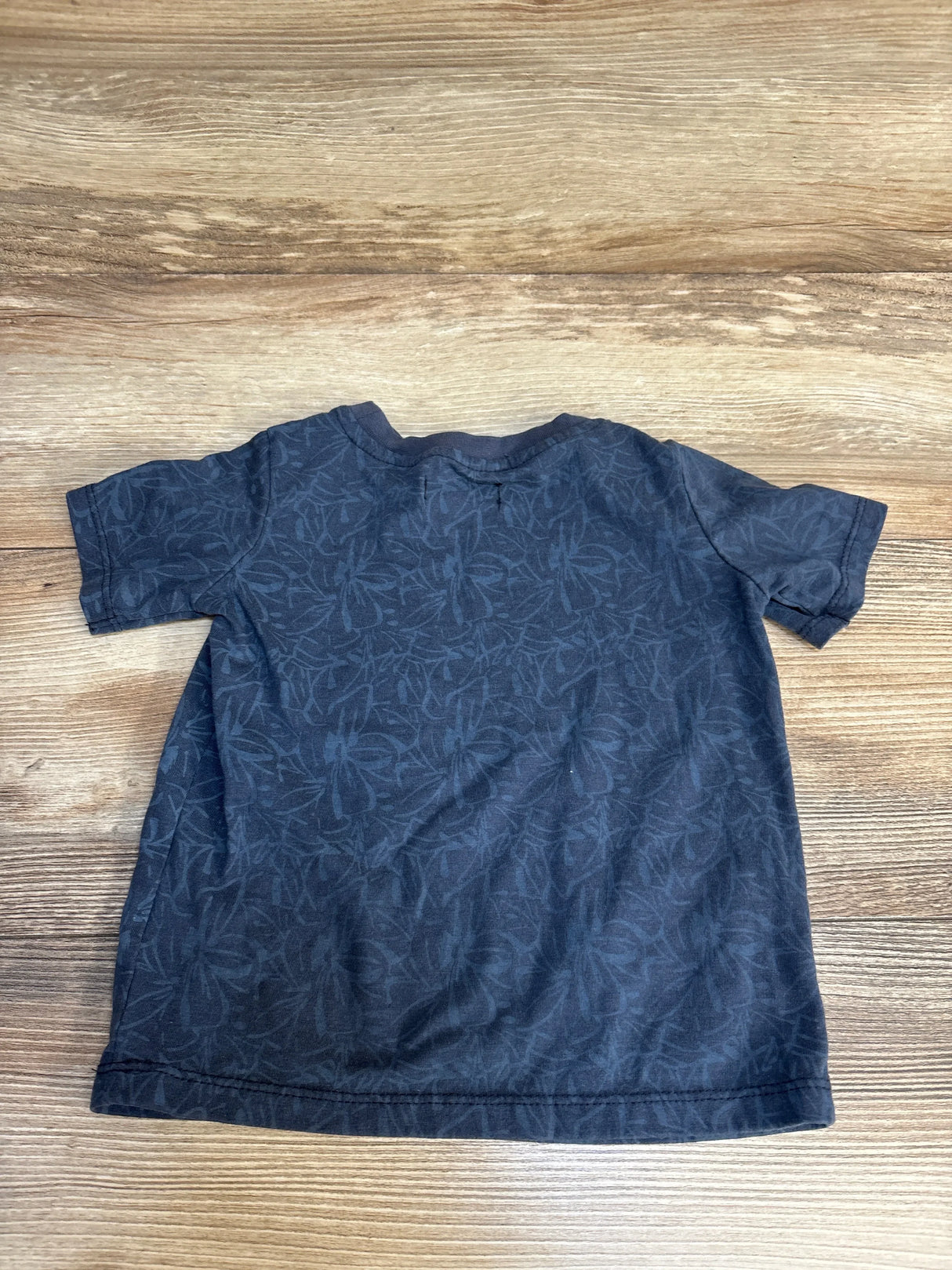 Navy blue toddler t-shirt with subtle floral print, laid flat on wood floor for kids clothing resale