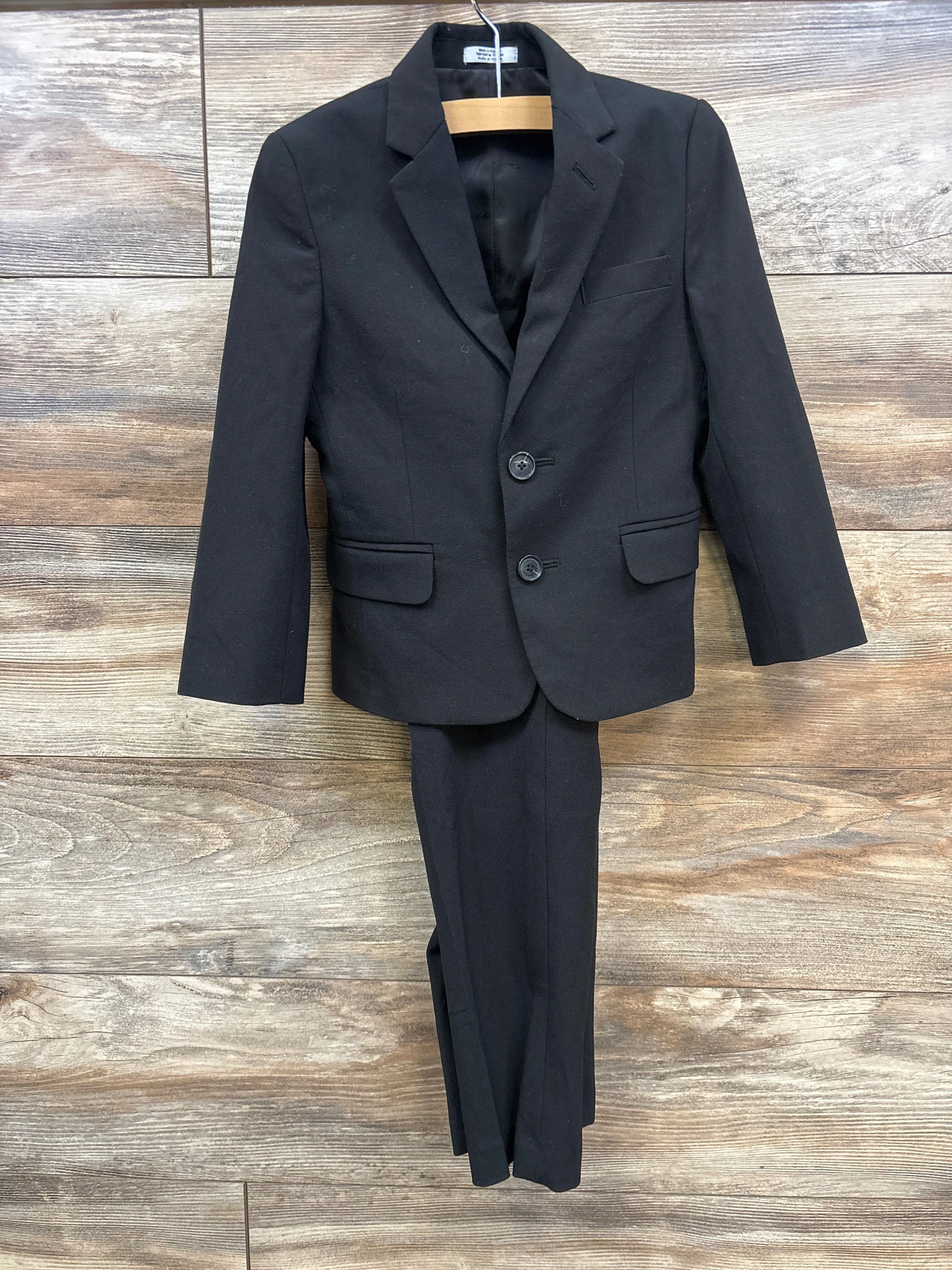 black two-button blazer and matching dress pants on wooden hanger over wood floor