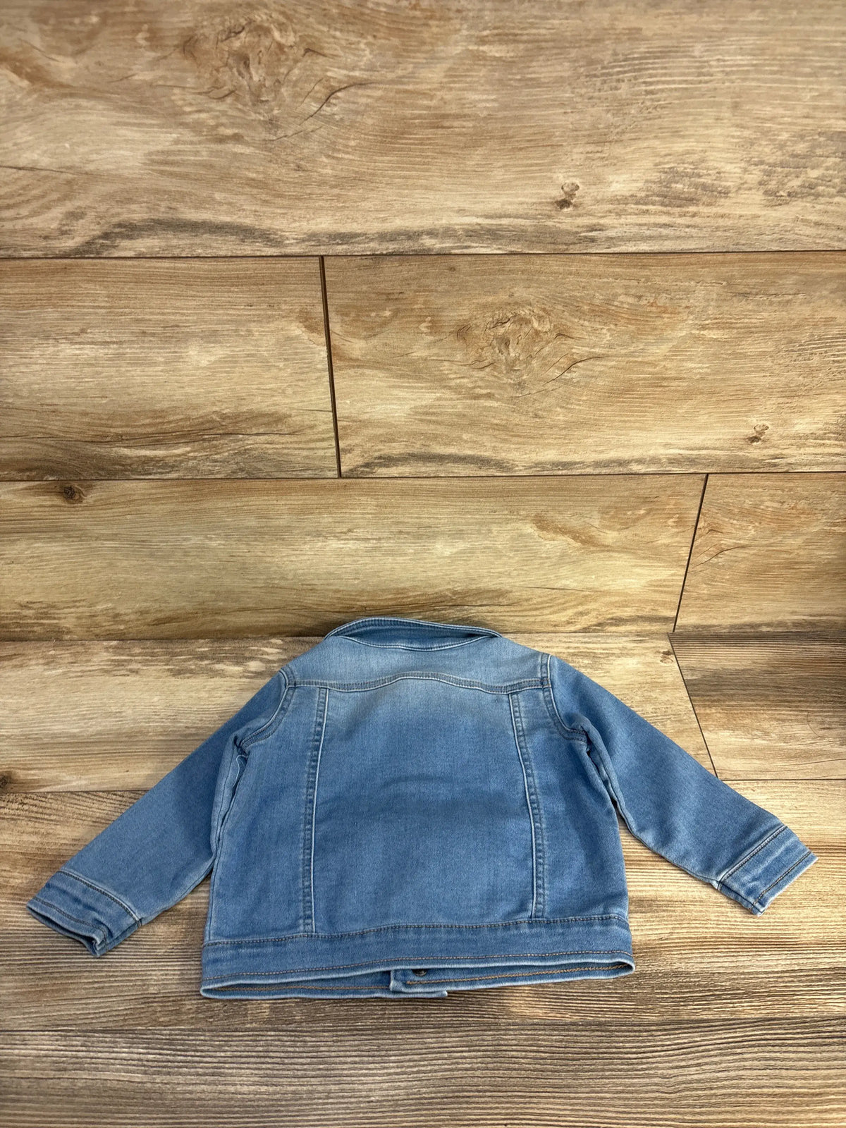 Back view of Cat & Jack blue denim jacket for 18 months showcasing long sleeves and stitched seams on a wood-grain floor