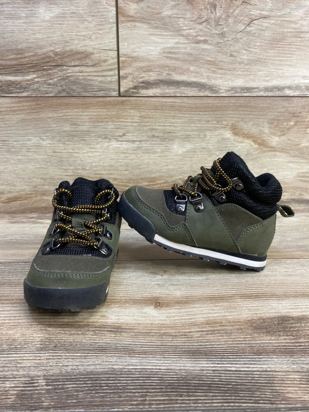 Pair of olive green and black toddler hiking boots with yellow laces on wooden floor
