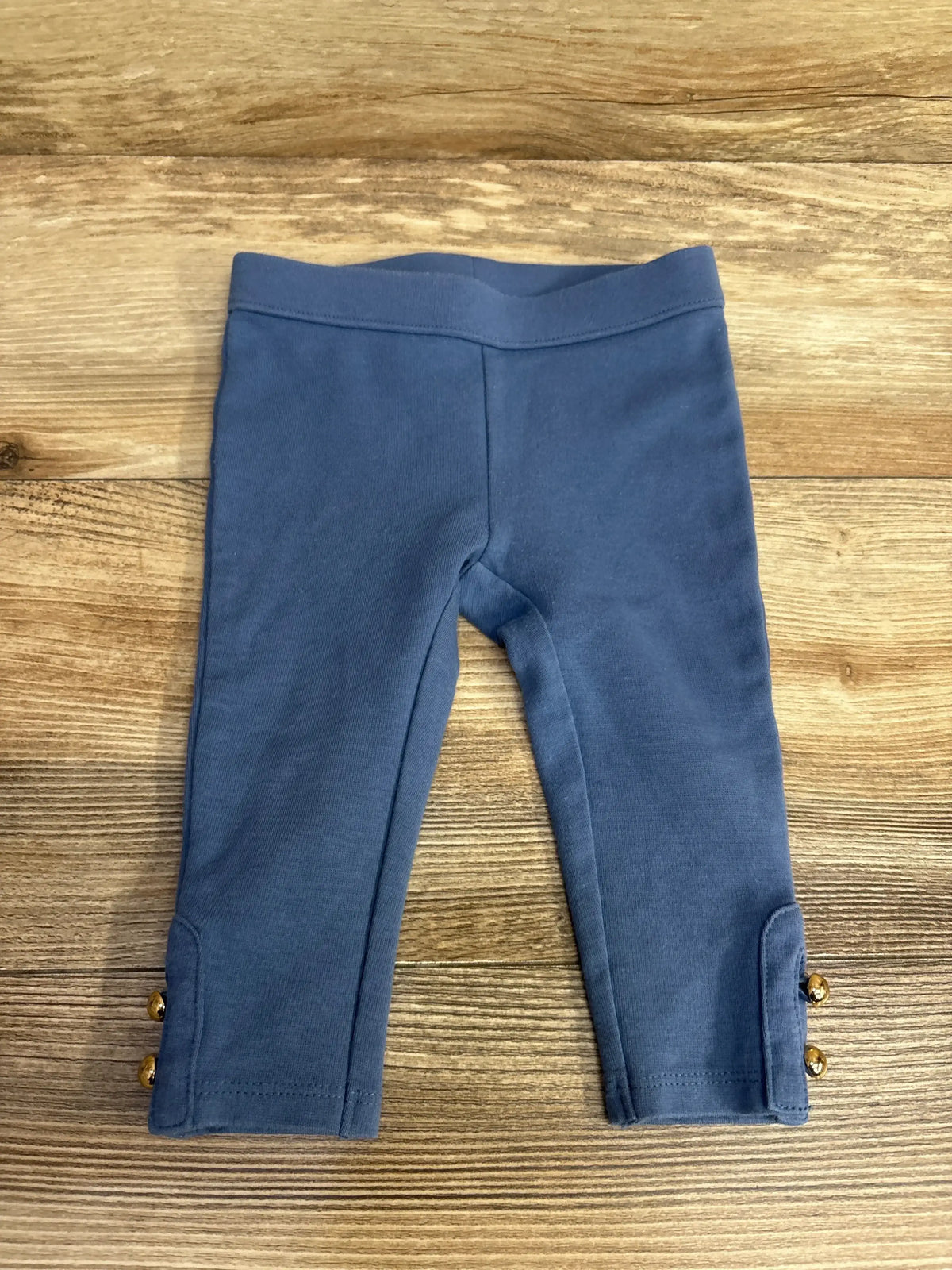 Flat lay of Janie & Jack River Run blue ponte pant size 6-12m showing gold button cuff details on wood surface