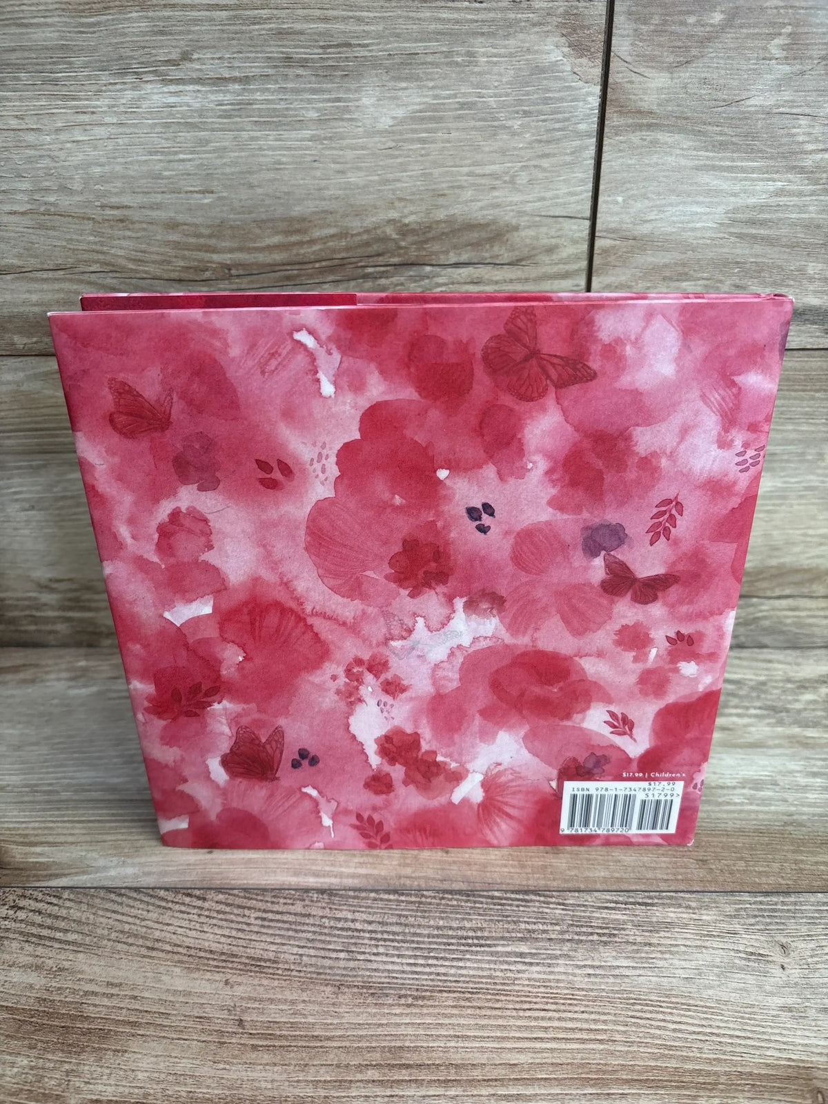 Children’s book with pink and red watercolor floral back cover, barcode visible, on wood.