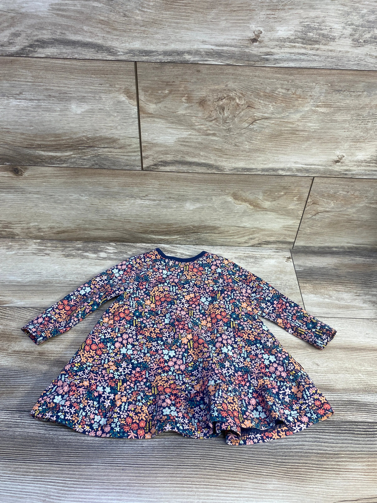 Flat-lay view of Tea navy long-sleeve floral dress showcasing a gathered waist and tiered skirt on a wood floor