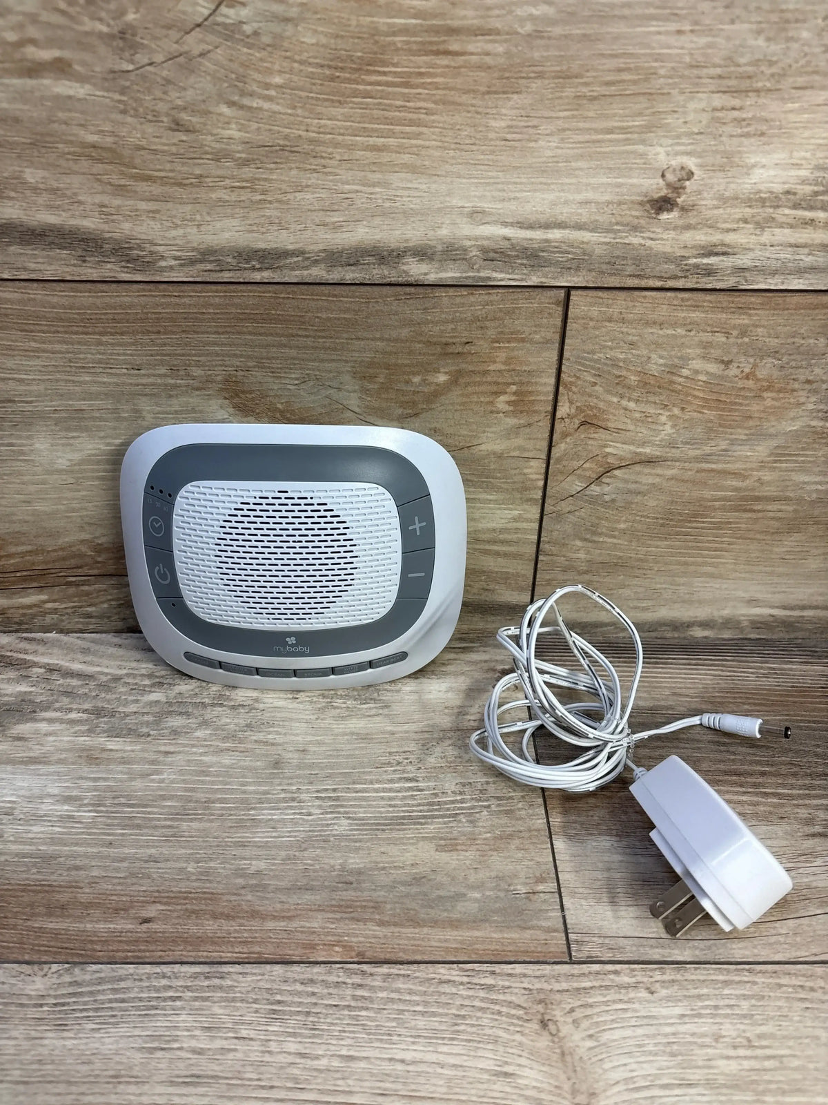 Front view of Homedics MyBaby SoundSpa portable sound machine showing speaker grille, control buttons, and included power adapter on wood background
