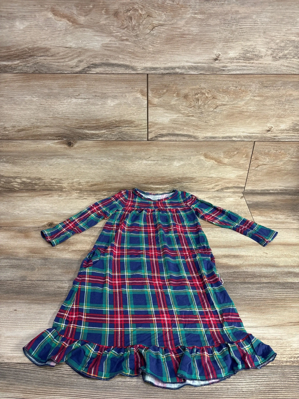 Plaid toddler dress with ruffled hem, festive red green blue pattern, long sleeves, laid on wood floor