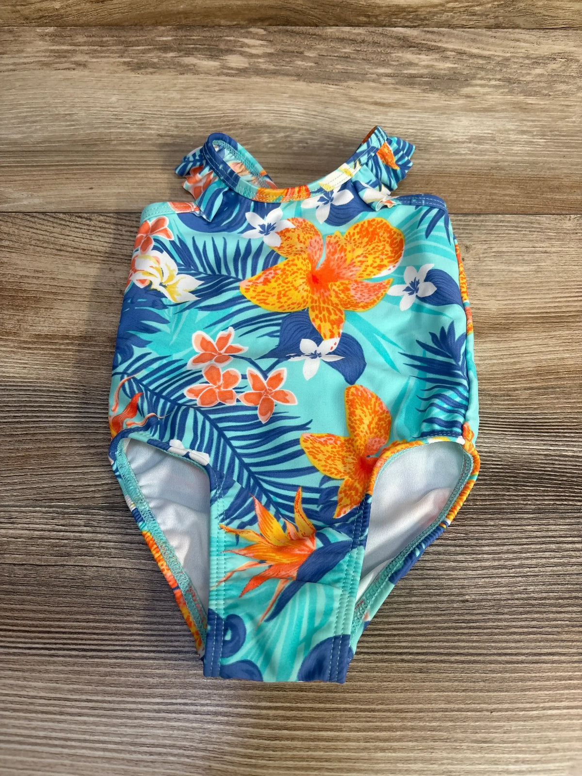 Flat lay of Children’s Place newborn one-piece swimsuit showing turquoise floral print and ruffle shoulder strap on wood surface