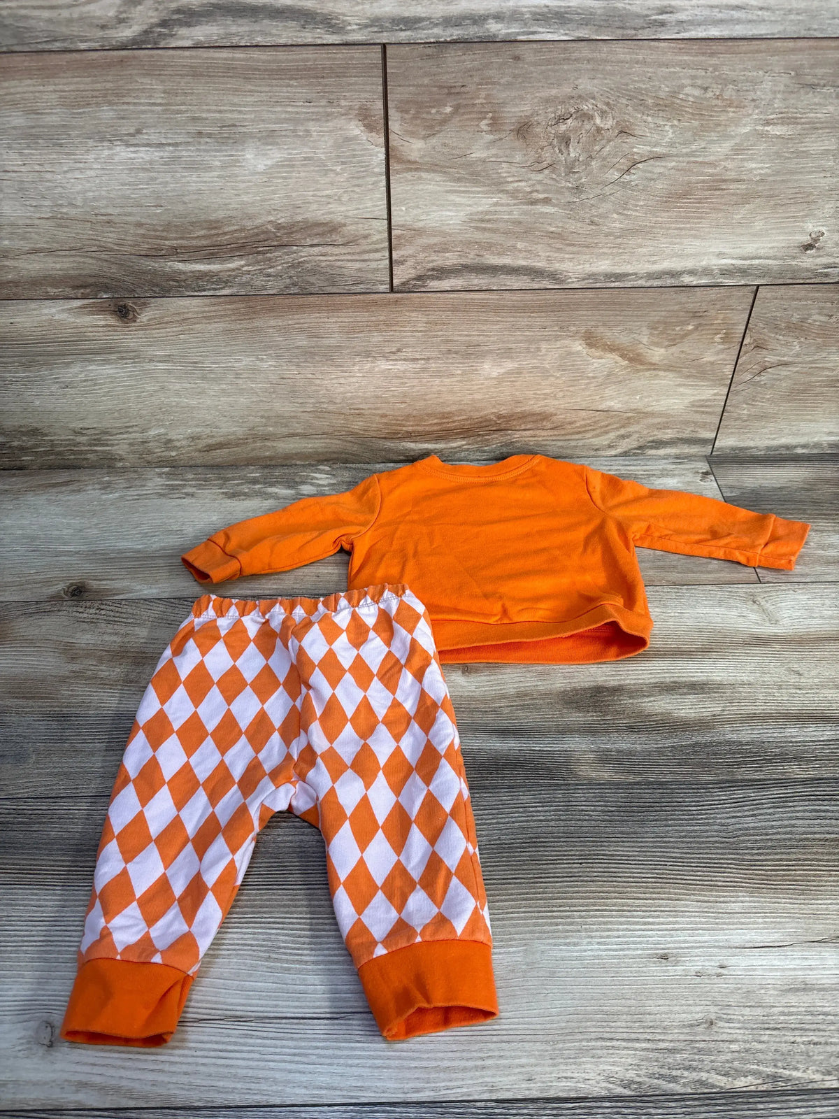 Top-down view of Cat & Jack orange sweatshirt and joggers set for 3 to 6 months, with diamond-patterned pants on wood