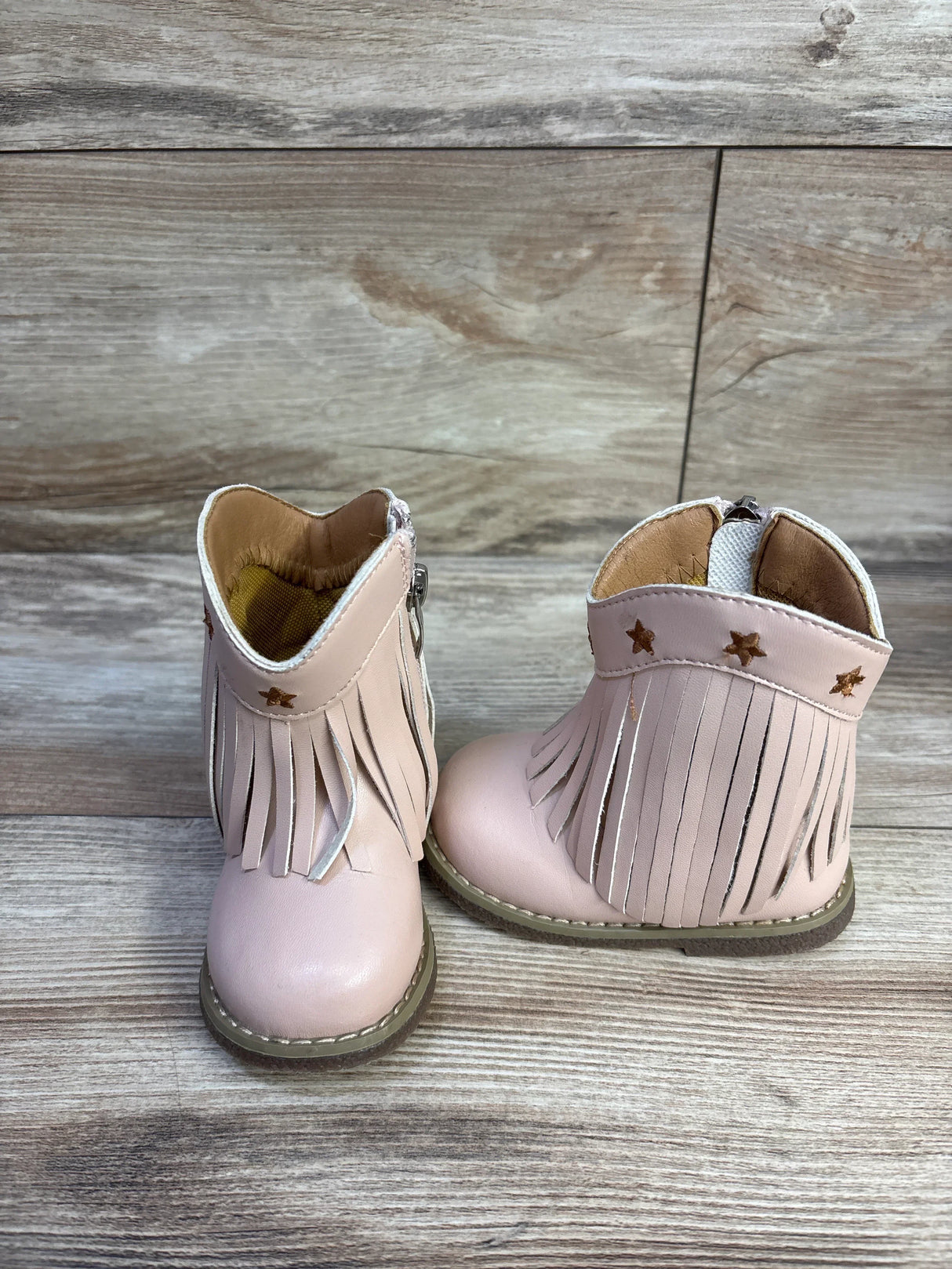 Front view of toddler pink round-toe western cowgirl boots showcasing fringe and metallic star accents on wood-look background