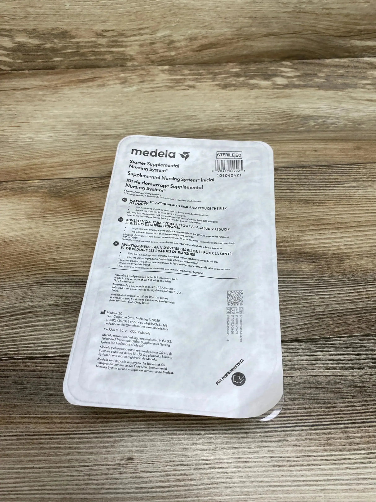 Angled top-down view of Medela Starter Supplemental Nursing System pouch showcasing front label and barcode on wood background