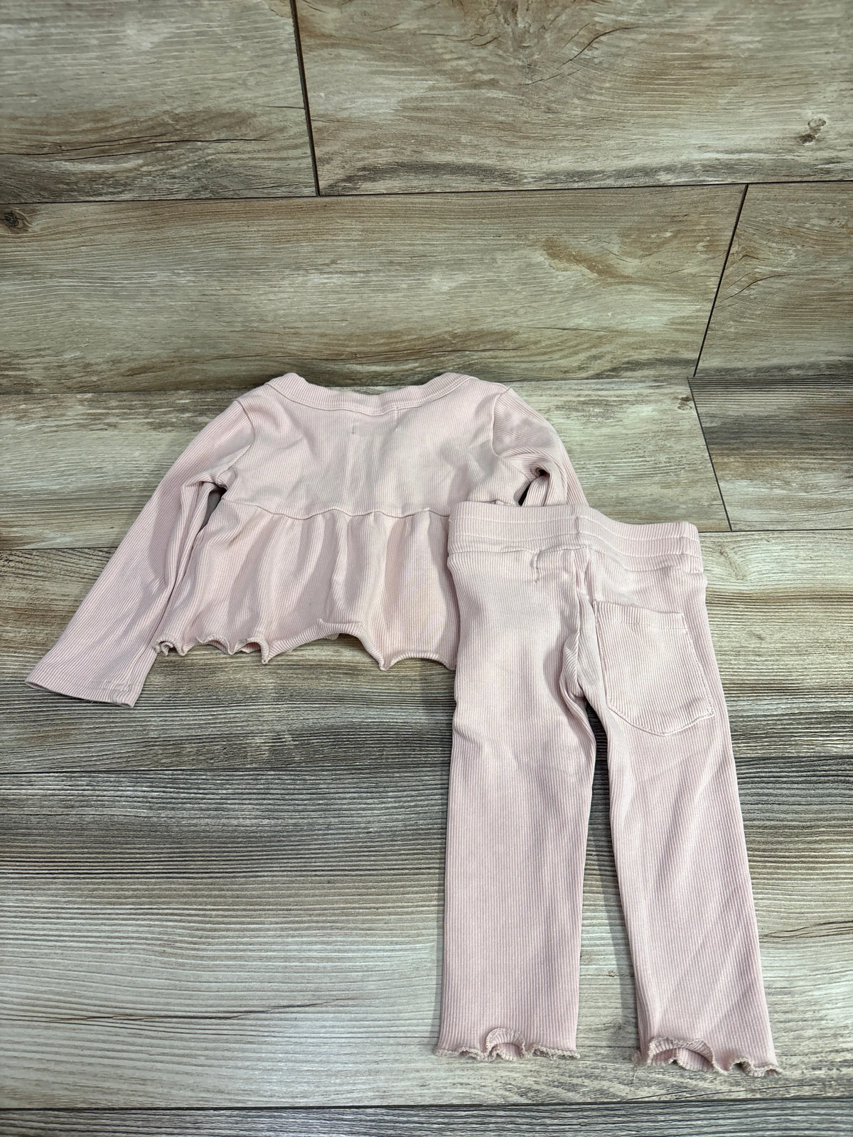 Flat lay of Fable and Ford pink ribbed long sleeve top and pants set with ruffled hems and back pocket on wood floor