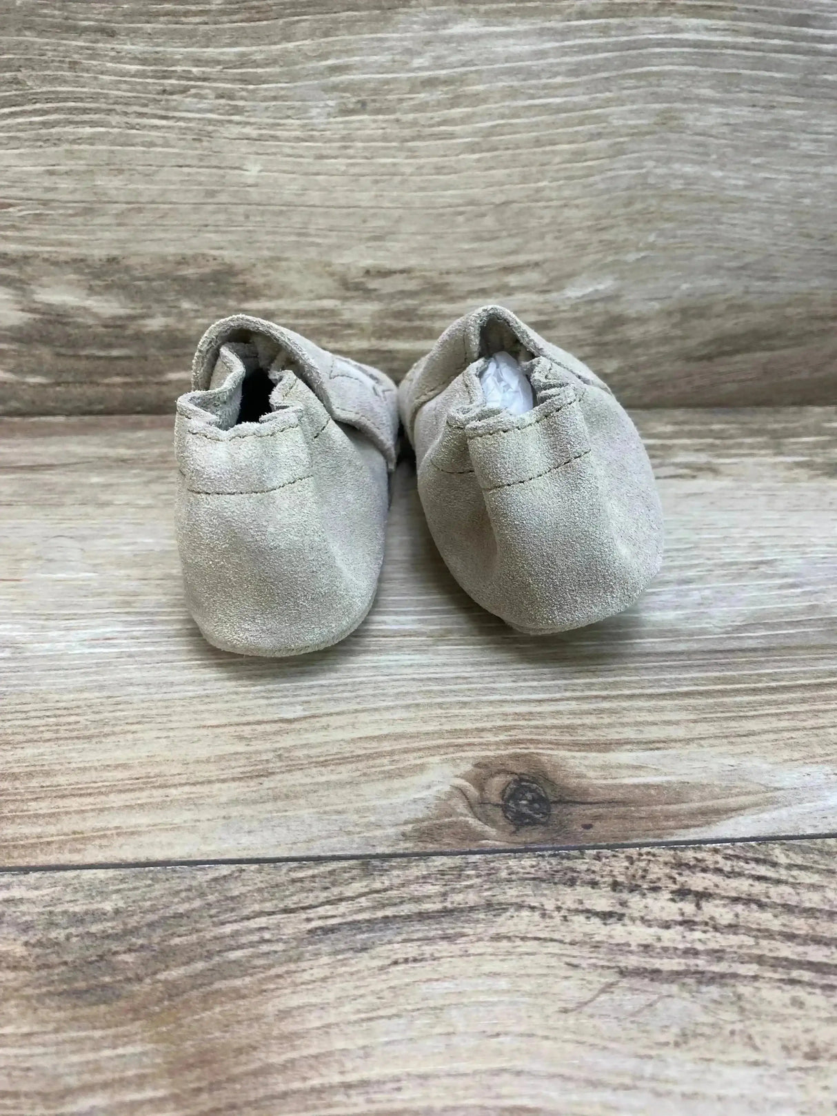 Rear view of Minnetonka Star infant booties showing tan suede material and elasticized heels on wood background