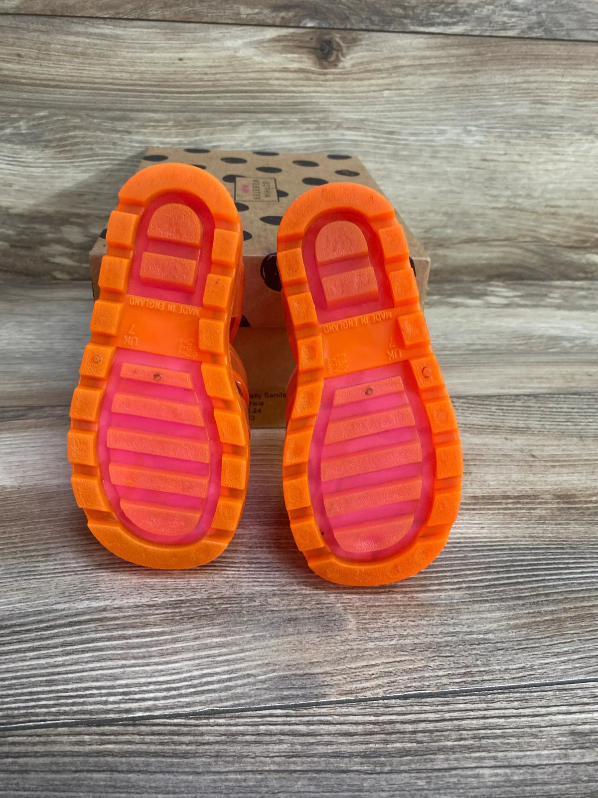 Bottom view of Sophia Webster butterfly jelly sandals showing orange soles and pink footbeds on a polka-dot shoebox