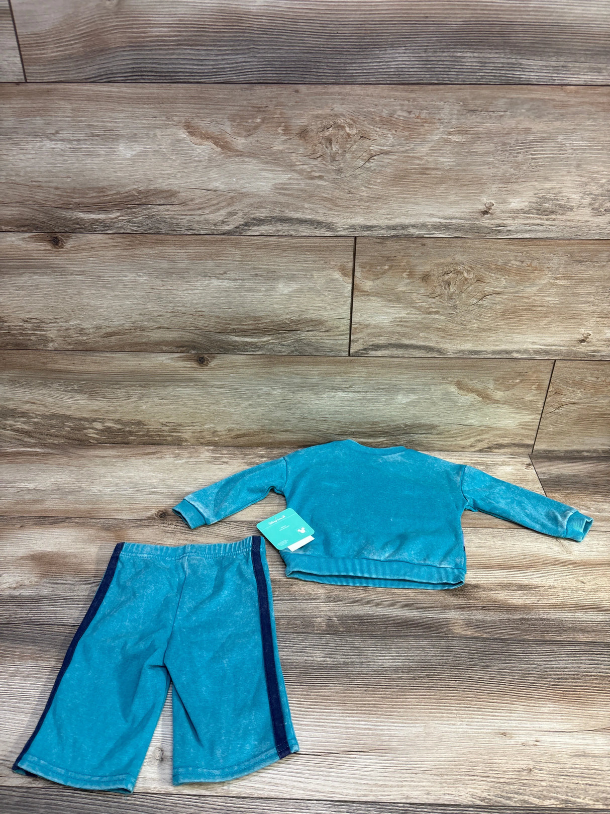 Flat lay back view of Disney Baby two piece Mickey Mouse pullover and shorts showing navy side stripe and new tag on wood background