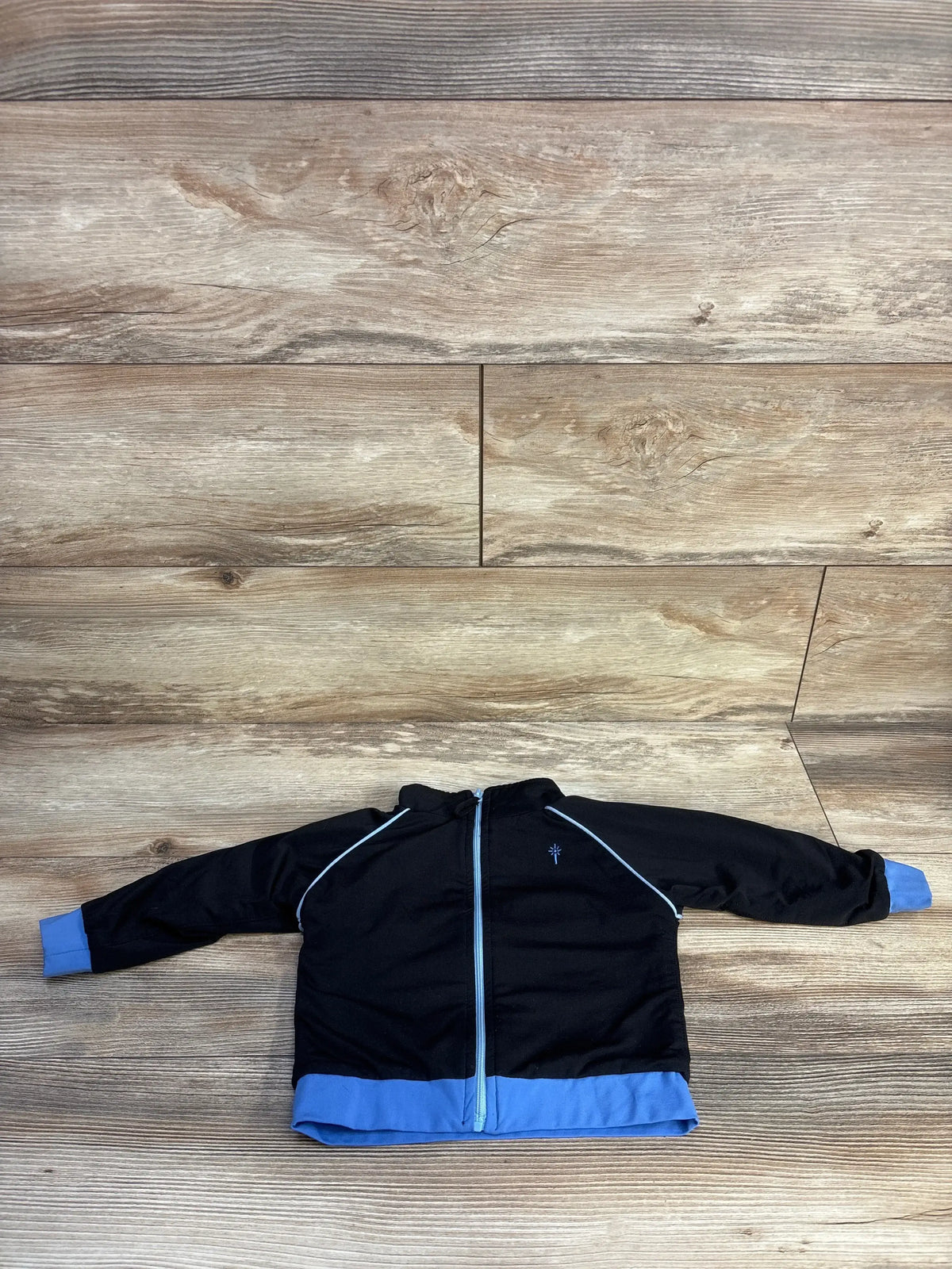 Front flat lay of iPlay zip-up jacket, black with blue cuffs and hem, center zipper and chest logo on wood background