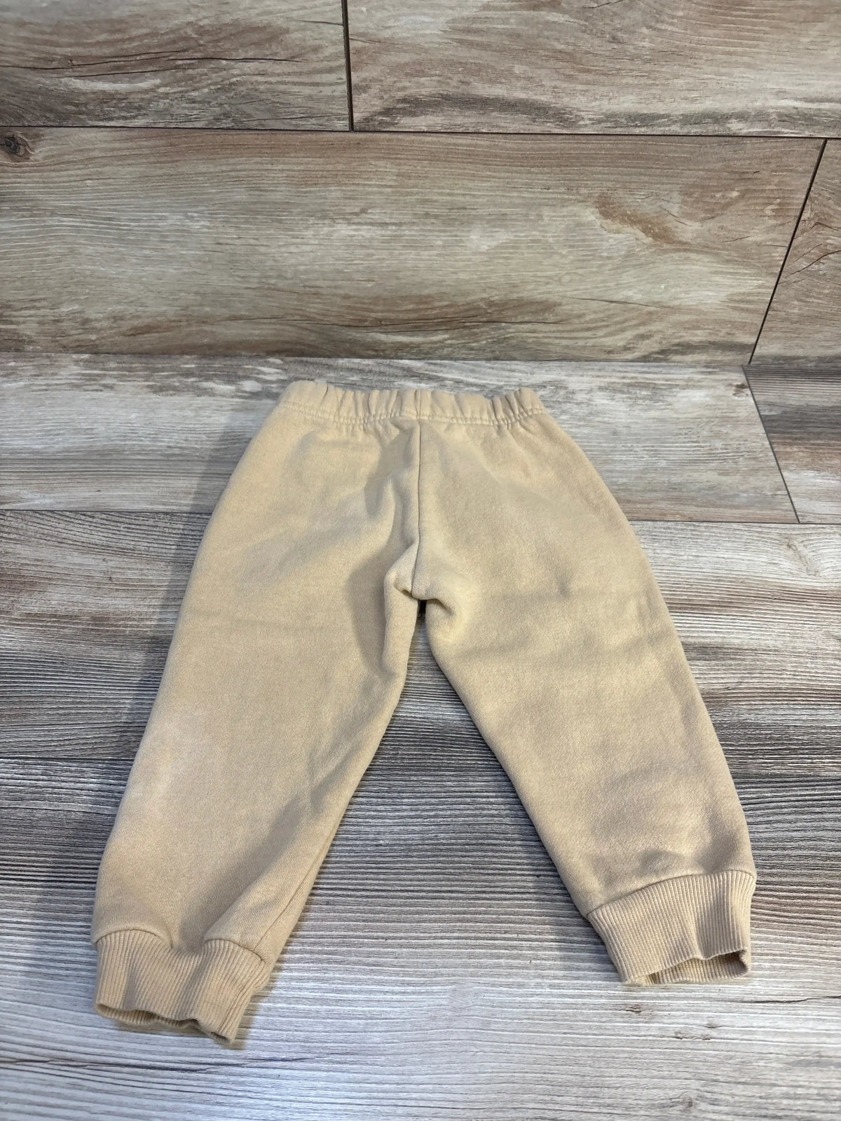 Back view of Champion beige toddler joggers showcasing elastic waistband and ribbed ankle cuffs on light wood background