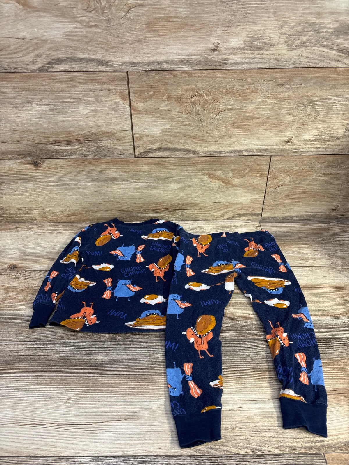 Flat lay of navy Carter’s 2-piece toddler pajama set (3T) showcasing pancakes, eggs, and bacon print on wood background