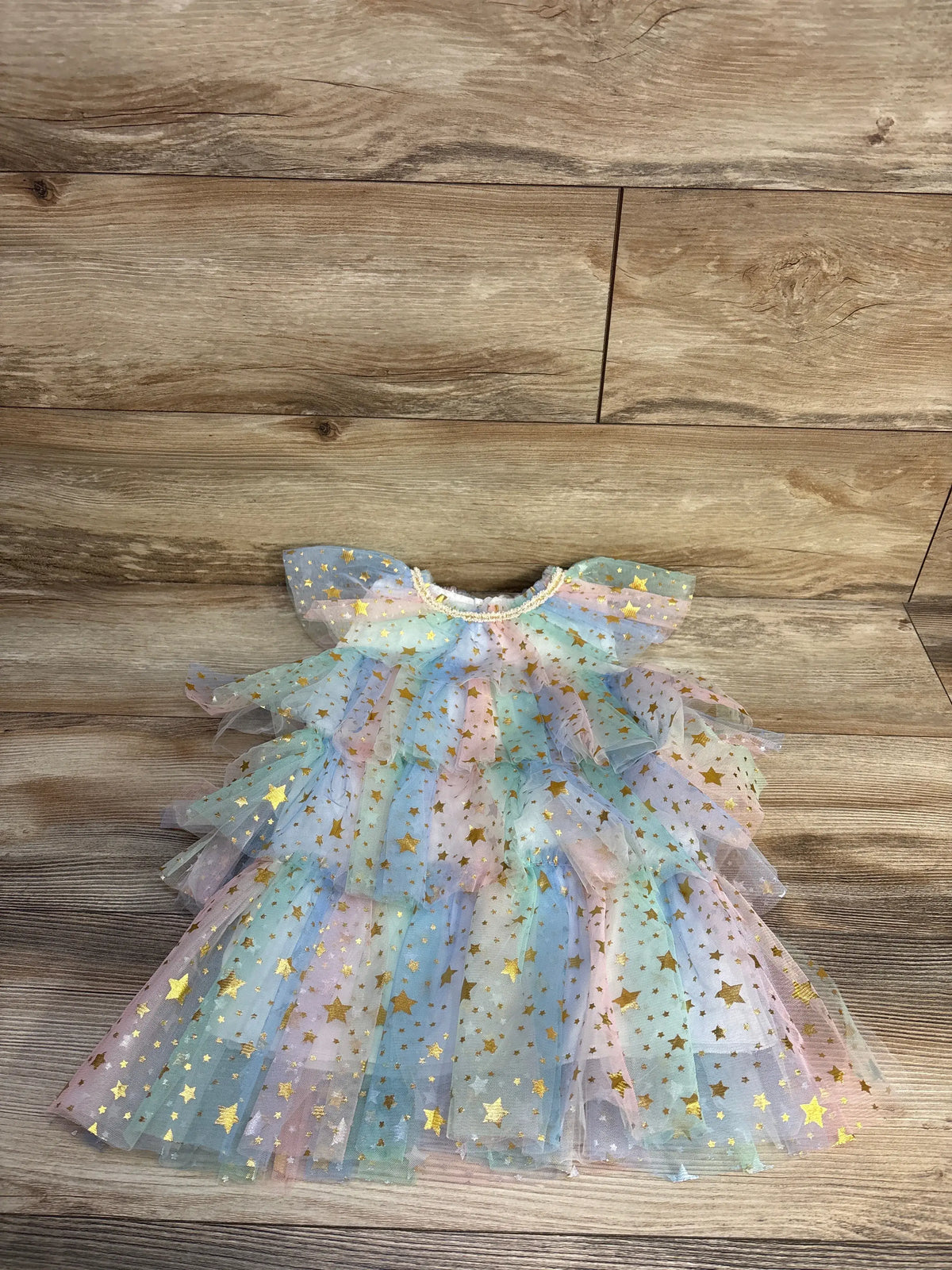Front view of white star print layered tulle dress showcasing layered tulle and gold stars on a wood floor