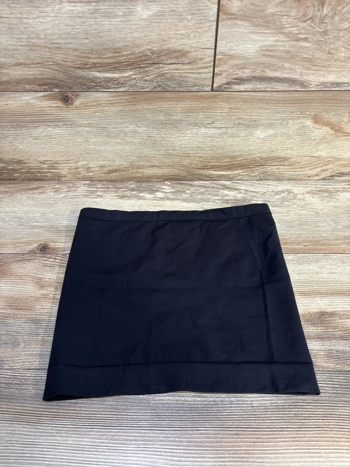 Flat lay of Ingrid and Isabel black maternity belly band, size S/M, tube-style stretch fabric with folded hem on wood floor