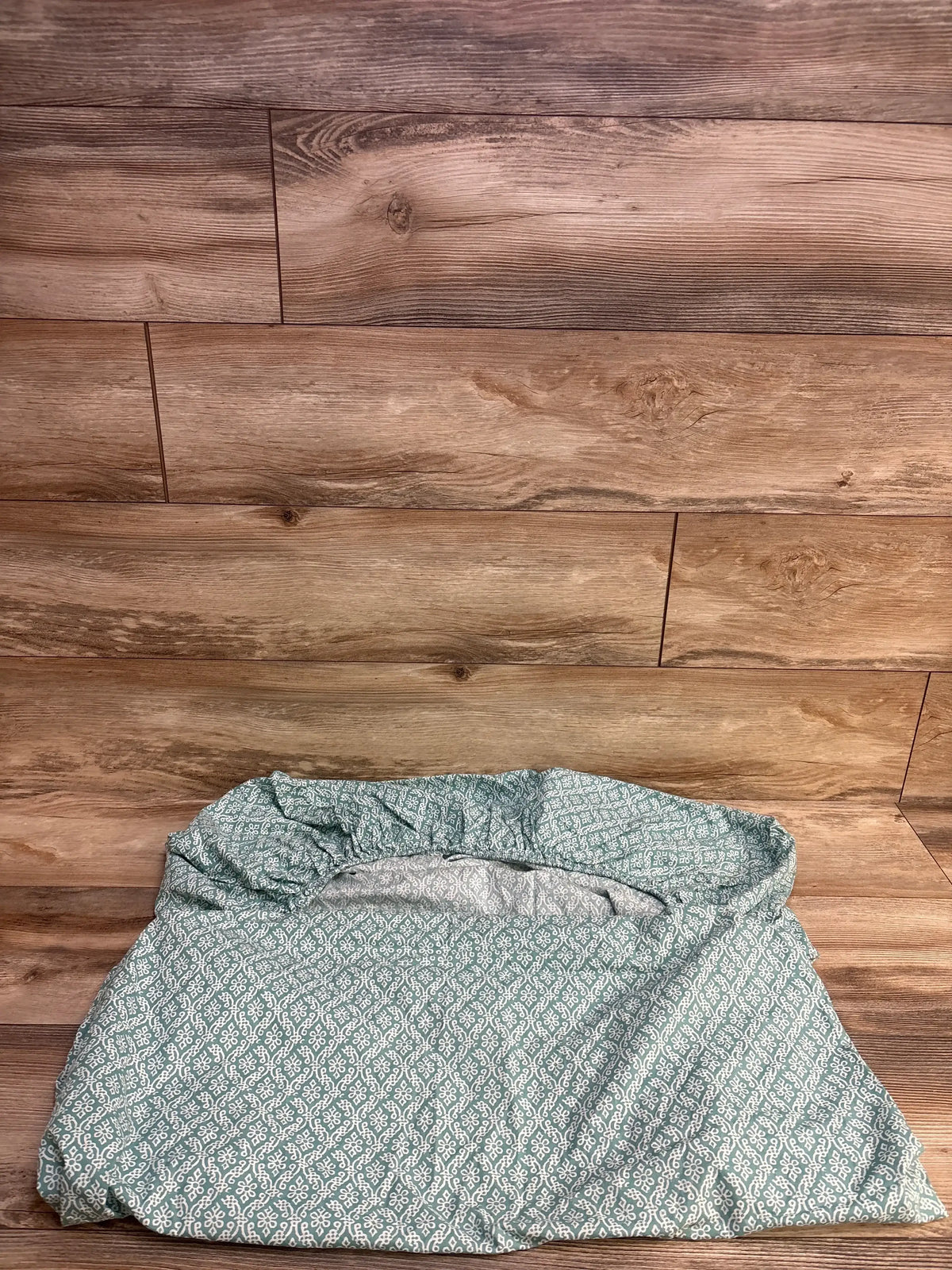 Top-down Levtex fitted crib sheet, sage green with white pattern, showing elastic opening on wood backdrop
