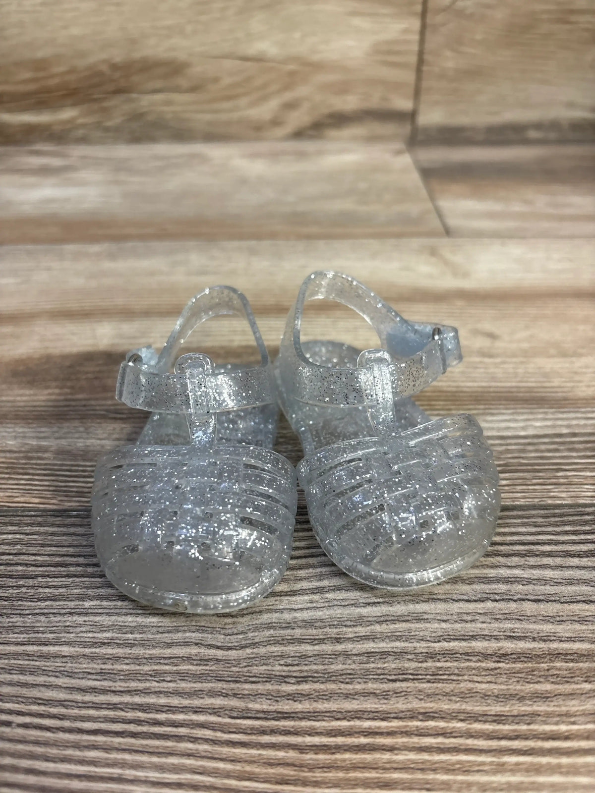 Front view of clear glitter Old Navy toddler jelly sandals with woven closed-toe straps and ankle buckle on wood background