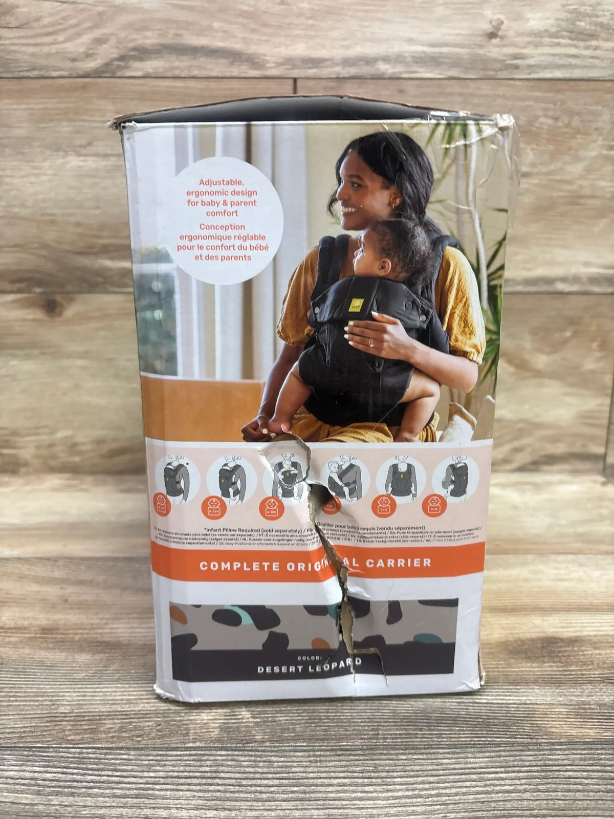 Front view of boxed NEW LILLEbaby Complete Original 6-in-1 Baby Carrier (Desert Leopard) showing packaging photo of parent wearing carrier and a torn, dented front on a wooden surface