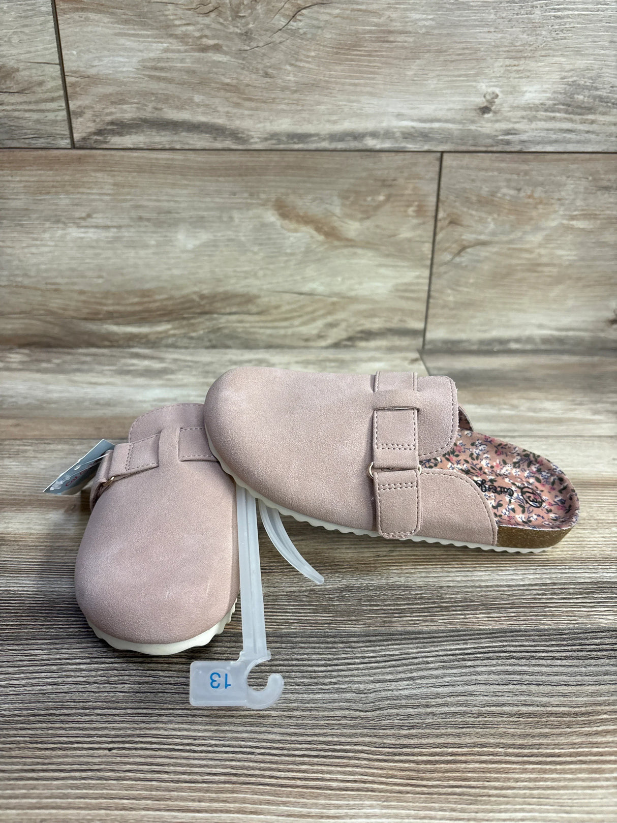 Pair of pink toddler slip-on clogs with adjustable strap and floral insole on wood surface, size 13