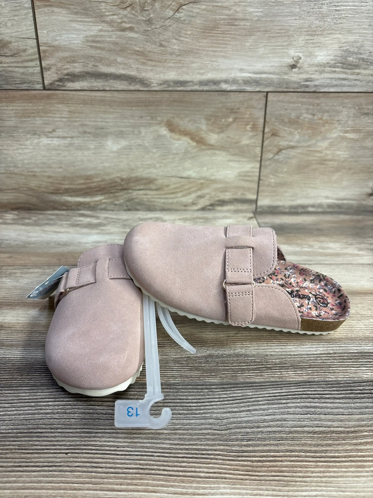 Pair of pink toddler slip-on clogs with adjustable strap and floral insole on wood surface, size 13