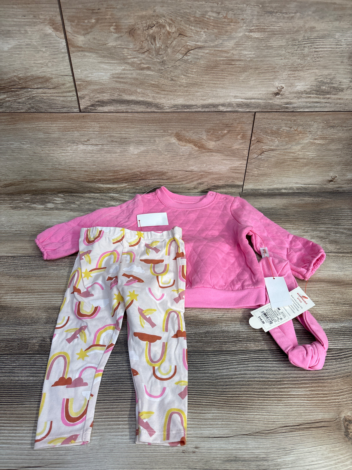 Pink quilted long sleeve top with tags and colorful patterned leggings on wood background