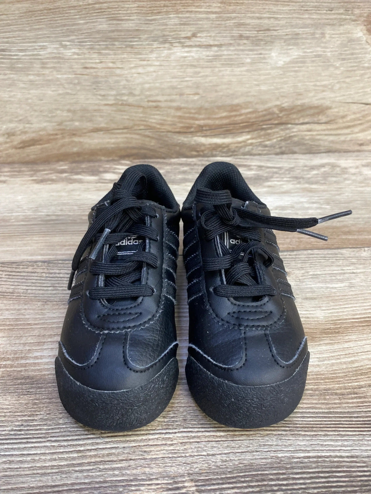 Black Adidas toddler sneakers on wood background, kids athletic shoes with laces.
