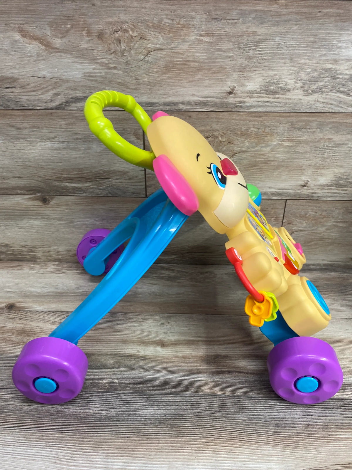 Side view of Fisher Price Laugh and Learn Smart Stages Puppy Walker with activity panel and colorful wheels on wood flooring
